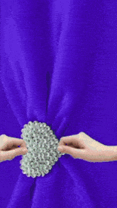 a person is holding a purple curtain with a pearl ring on it
