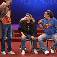 a man wearing a superman shirt talks to two other men on a stage