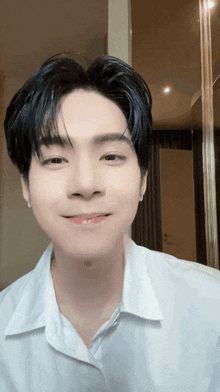 a young man wearing a white shirt is smiling and looking at the camera