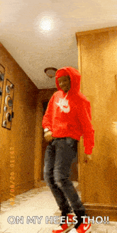 a man in a red hoodie is dancing in a hallway with the words `` on my heels tho '' .