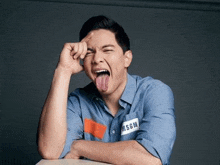 a man in a blue shirt is sticking his tongue out and making a funny face .