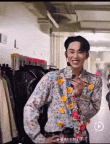 a young man wearing a floral shirt and tie is smiling in a room with clothes hanging on a rack .