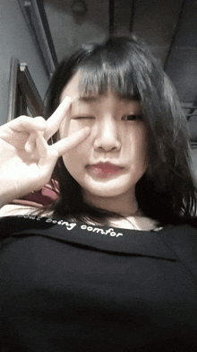 a woman wearing a black shirt that says being comfort makes a peace sign