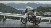 a woman holding an umbrella stands next to a man on a kawasaki motorcycle