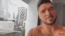 a shirtless man stands on a balcony with a subscribe button on the bottom right