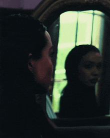 a woman looks at her reflection in a mirror with her eyes closed