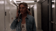 a woman in a denim jacket is talking on a cell phone while walking down a hallway .
