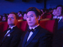 a man in a tuxedo sits in a theater watching a movie