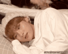 a young man wearing a hat and a white shirt is laying on a bed .