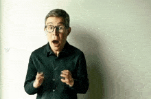 a man in a black shirt and glasses is making a surprised face .
