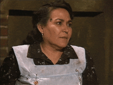 a woman wearing a blue apron and earrings looks serious