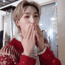 a young man wearing a red sweater is blowing a kiss