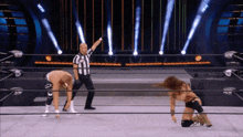 a referee stands between two wrestlers in a wrestling ring with the letters aew on the ring