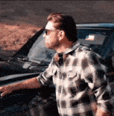 a man in a plaid shirt stands next to a car