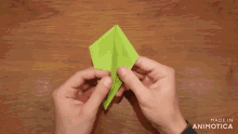 a person is holding a green origami piece with the words made in animotica below it
