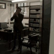 a man in a suit stands in front of a bookshelf talking on a cell phone