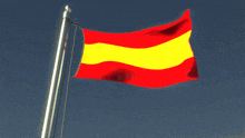 a red and yellow flag is waving in the wind against a blue sky