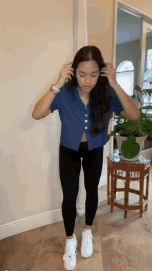 a woman in a blue shirt and black leggings is standing in a room