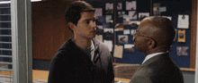a man in a suit and glasses talks to a young man in a hoodie