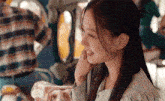 a young woman is sitting at a table in front of a merry go round and smiling .
