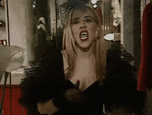 a woman in a black dress with a veil on her head is singing into a microphone