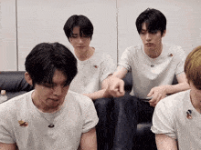 a group of young men are sitting on a couch and one of them has a necklace with a bird on it