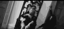 a black and white photo of a woman sitting on a throne in a room .