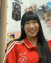 a woman with long black hair is wearing a red shirt with the letter r on it .