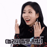 a woman with a surprised look on her face is holding her hands up in the air .