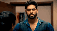 a man with a beard is wearing a blue shirt and a black vest