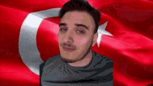 a man with a beard is smiling in front of a turkish flag
