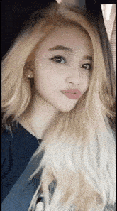 a woman with long blonde hair is wearing a blue shirt and earrings