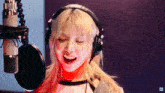 a blonde woman wearing headphones is singing into a microphone .