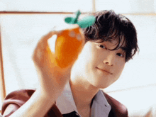 a young man is holding an orange in front of his face and smiling