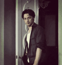 a man in a black jacket is standing in a doorway holding a black bag .