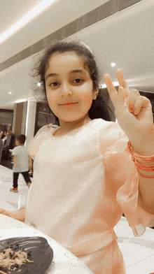 a little girl in a pink dress gives the peace sign