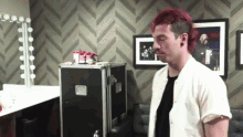 a man with red hair is standing in a dressing room in front of a mirror and a case .