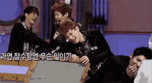 a group of young men are laughing and hugging each other while sitting around a table .