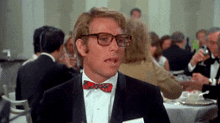a man wearing glasses and a bow tie is sitting at a table with other people