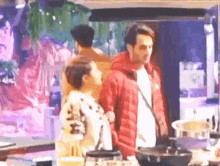 a man in a red jacket is standing next to a woman in a kitchen