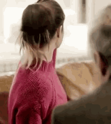a woman in a pink sweater is sitting on a couch next to a man in a suit .