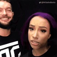 a woman with purple hair is standing next to a man with a beard and smiling .