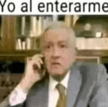an old man in a suit and tie is talking on a cell phone .