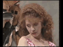 a woman with red curly hair is wearing a pink dress and looking at the camera .