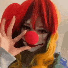 a woman dressed as a clown is holding a red nose in front of her face .