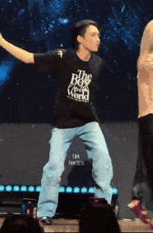 a man in a black shirt that says the boy from the world is dancing on a stage