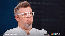 a man wearing white glasses and a chef 's jacket with the nbc logo on the bottom