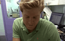 a man wearing a green polo shirt is sitting in front of a laptop