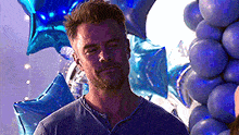 a man is standing in front of a bunch of blue balloons and looking at the camera .