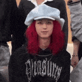 a woman with red hair is wearing a white hat and a black hoodie .